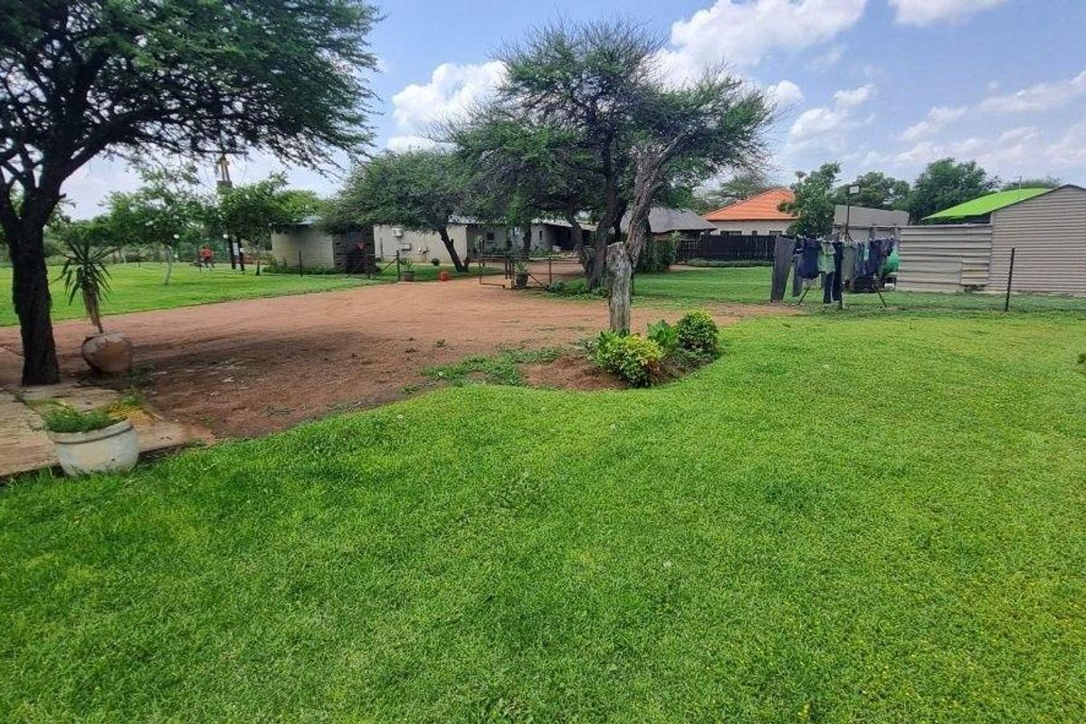 A spacious farm property featuring a large green lawn, established trees, a gravel driveway, and an outbuilding in the background.