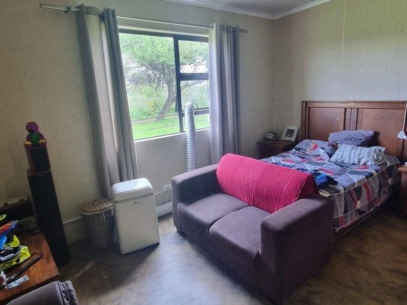 A bedroom featuring a window with aluminium frames and standard cornicing, currently showing signs of wear on the wall surfaces.