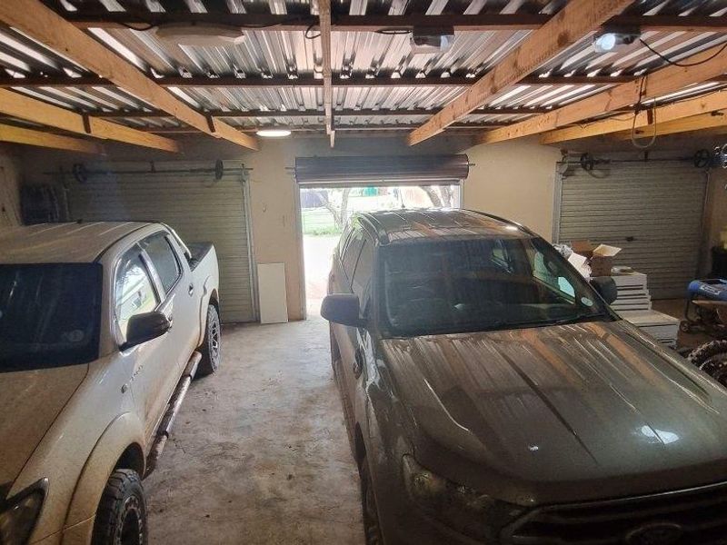 Spacious double garage featuring exposed timber rafters, corrugated metal roofing, and dual roller shutter doors with concrete flooring.