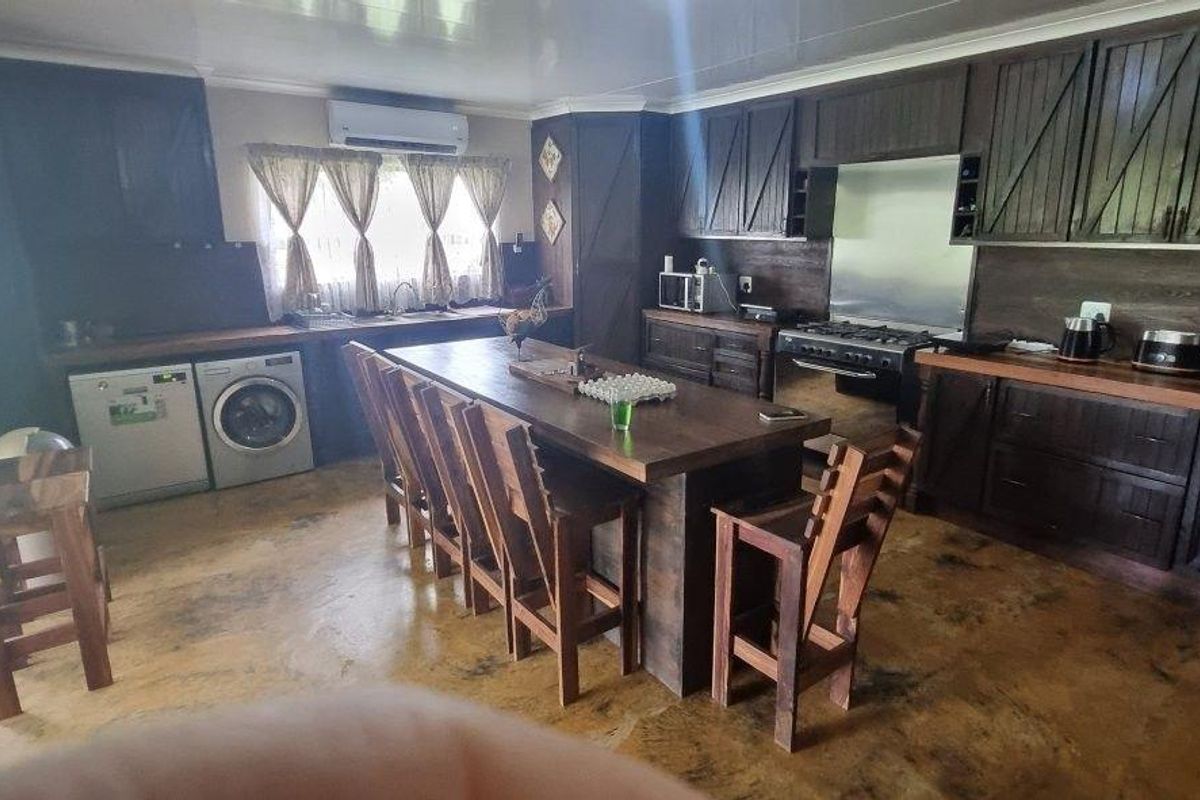 Spacious rustic-style kitchen featuring dark wood cabinetry, a large central island, integrated appliances, and direct access to the outdoor area.