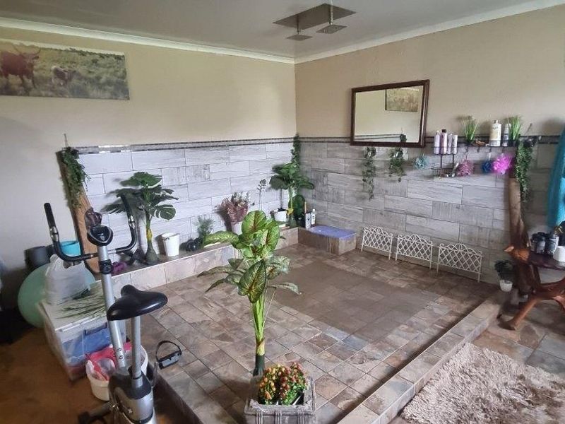 A spacious bathroom featuring a raised platform area, tiled wall finishes, and a ceiling-mounted shower head, currently utilized as a multi-purpose space.