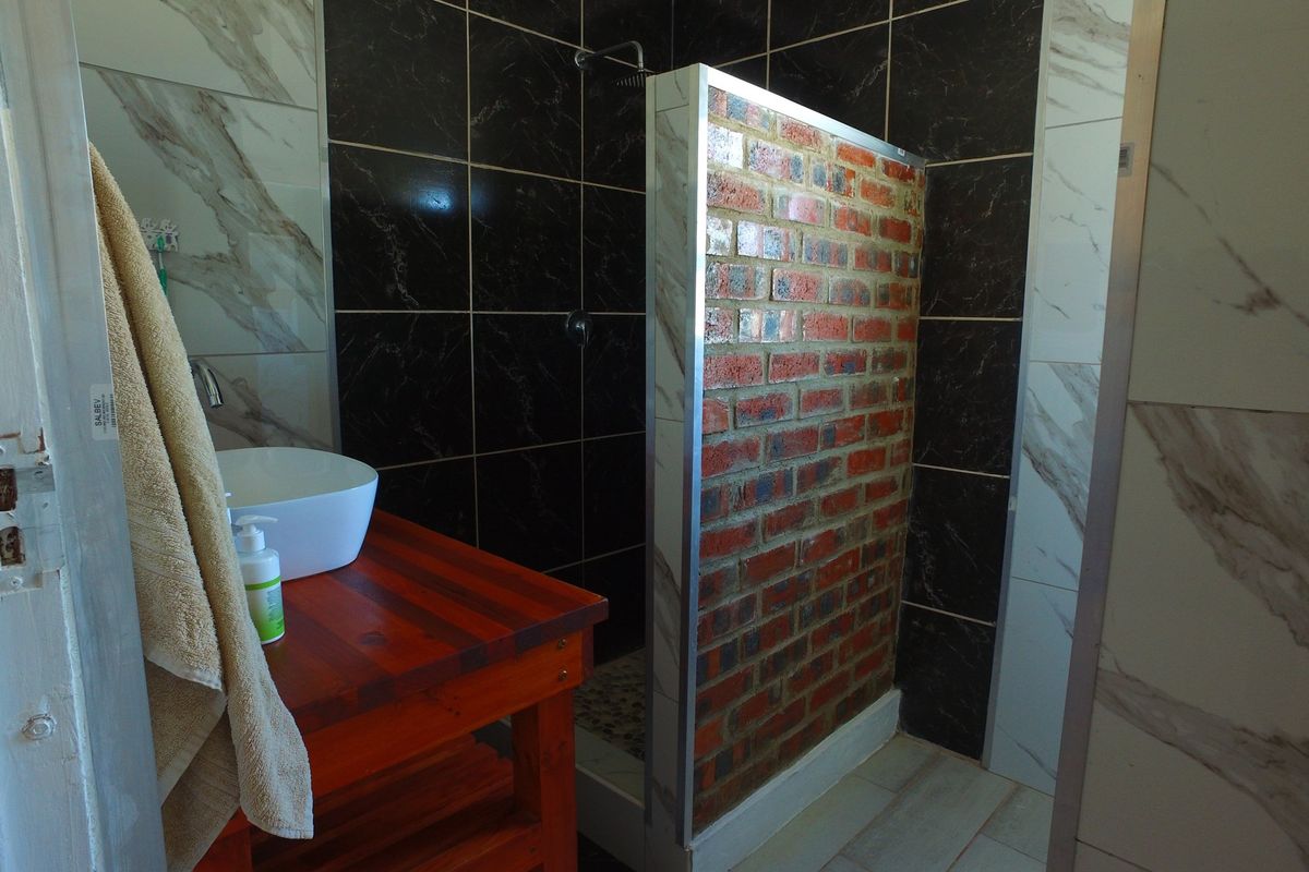 Modern bathroom featuring a vessel sink on a wooden vanity and a walk-in shower with contrasting black and marble-effect wall tiles.