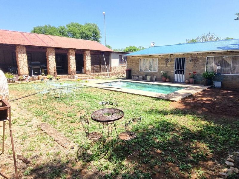 Rear garden area featuring a swimming pool, stone-clad structures, a covered patio, and a built-in brick pizza oven.