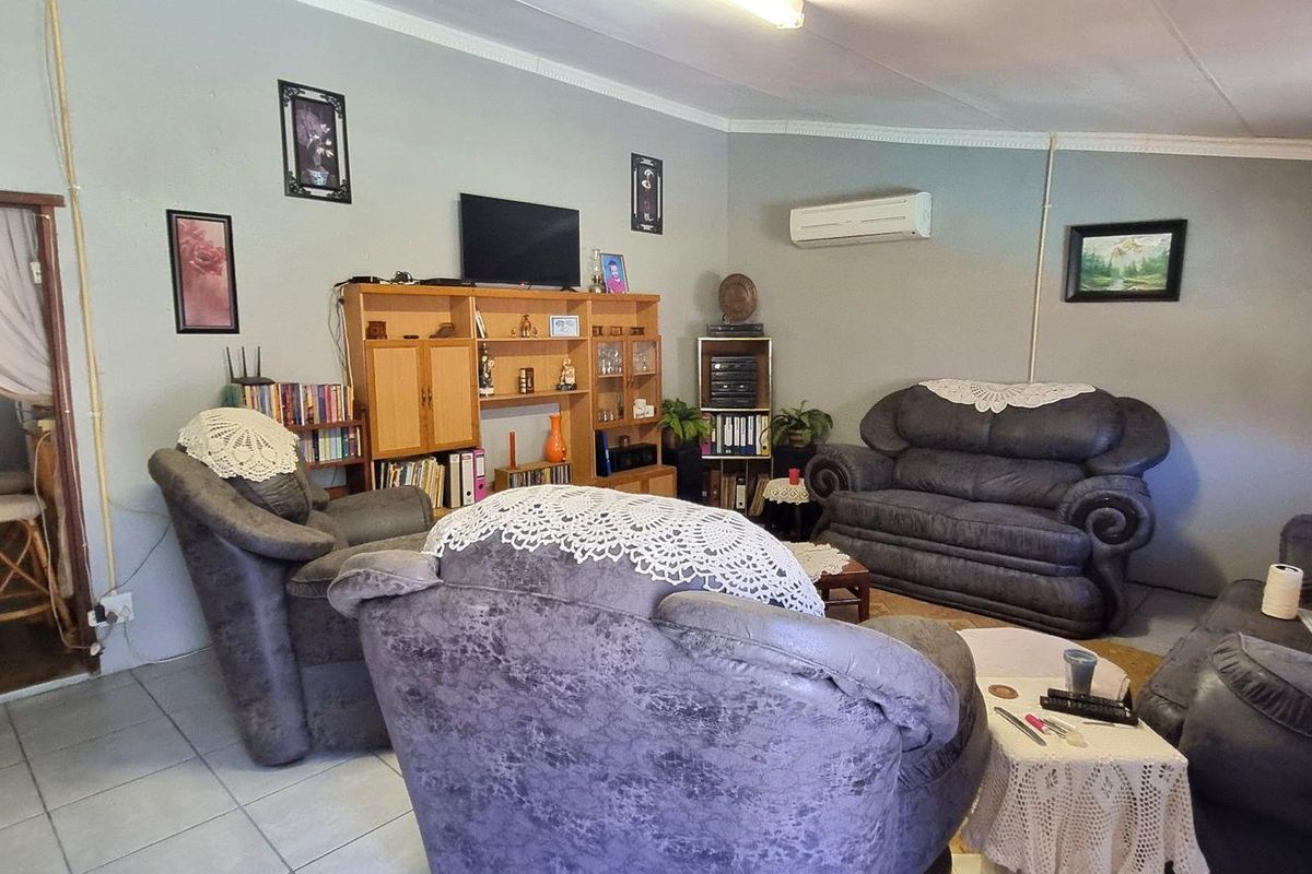 Spacious living room featuring tiled flooring, coved ceilings, and a wall-mounted air conditioning unit, with direct access to the adjacent kitchen area.