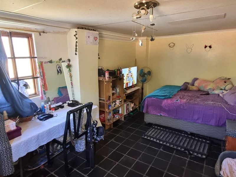 A bedroom featuring dark tiled flooring and a central ceiling light fixture, requiring some cosmetic updates to the walls and ceiling.