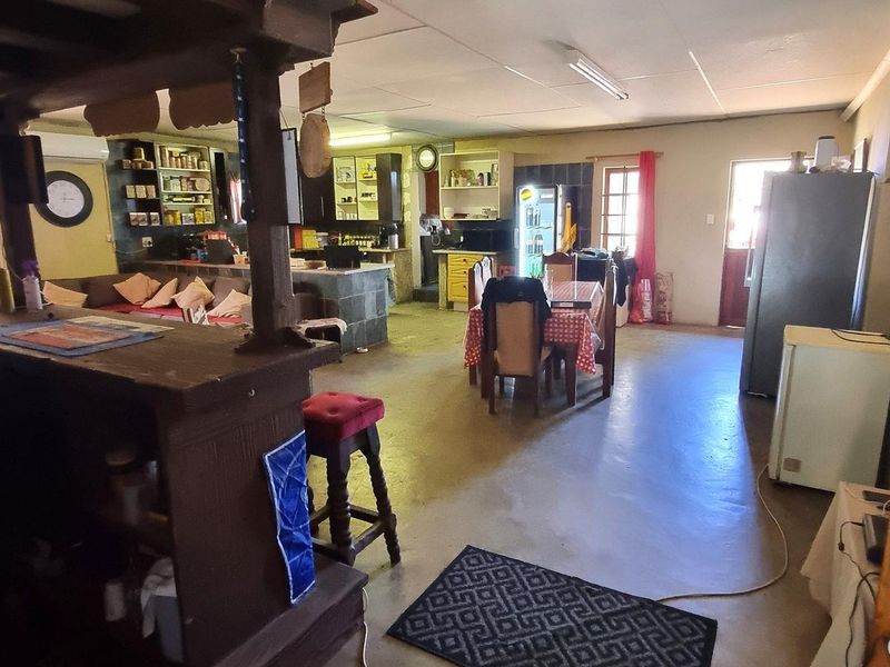 Spacious open-plan living area featuring a built-in bar, exposed timber ceiling beams, and a functional kitchen layout with concrete flooring throughout.