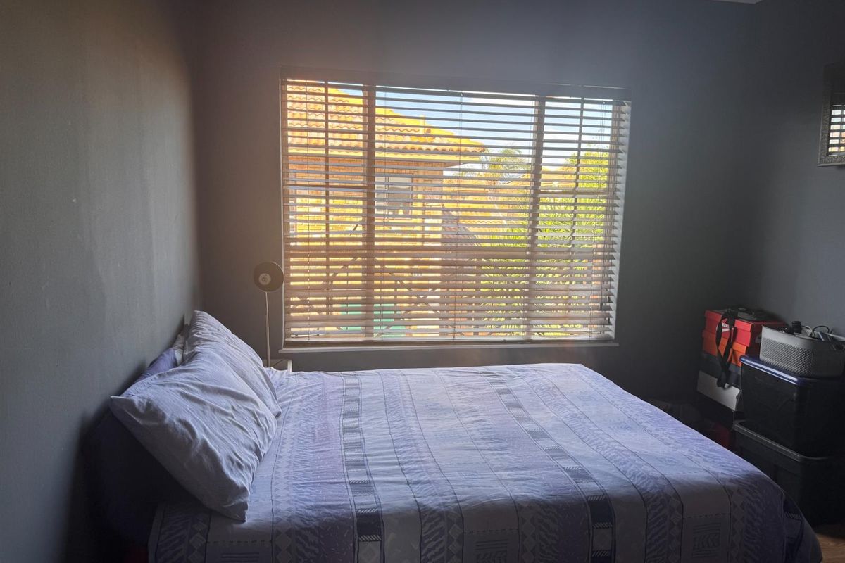 A bedroom featuring laminate flooring and fitted venetian blinds, offering natural light and a view of the surrounding townhouse complex.