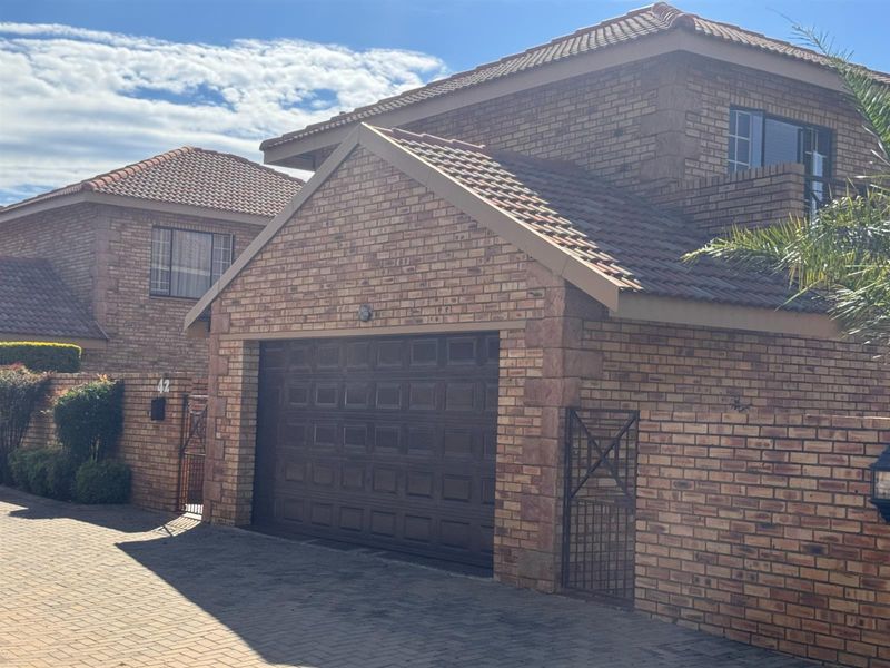 Front elevation of a face brick townhouse featuring a double garage, tiled roof, and paved driveway access.