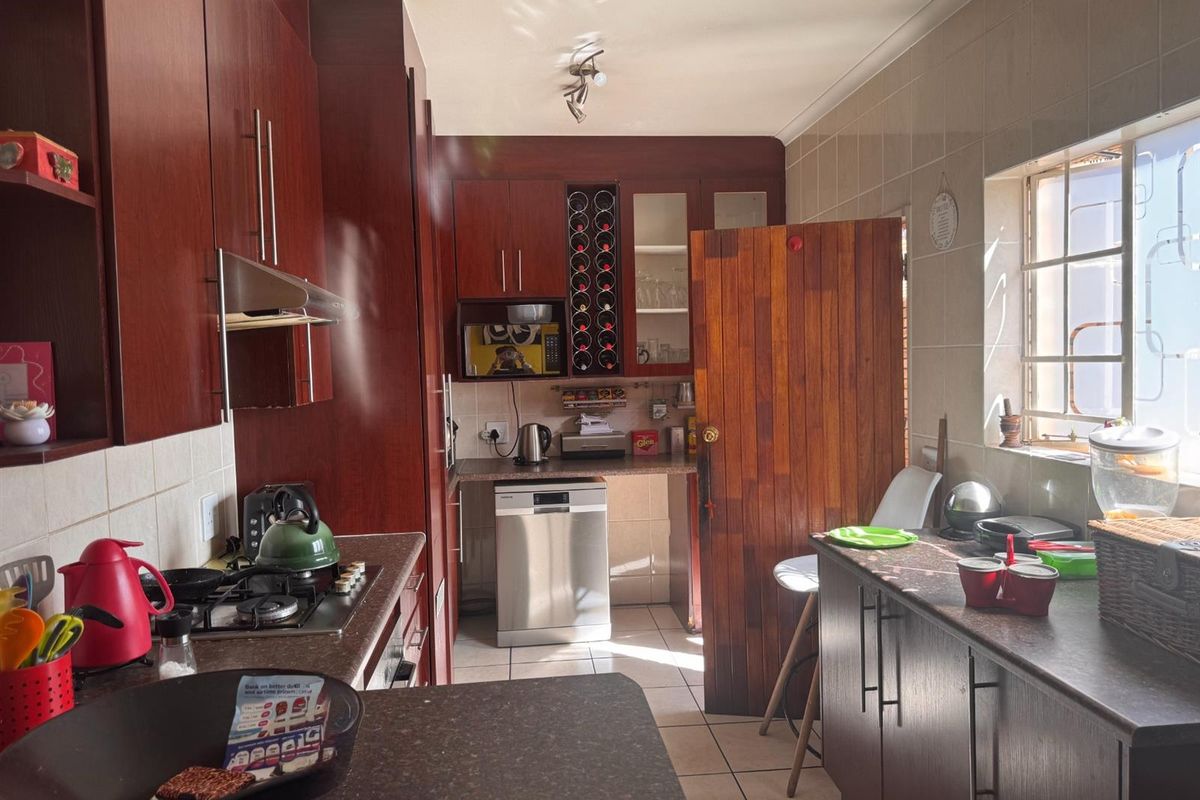 A functional kitchen featuring dark wood cabinetry, tiled splashbacks, a gas hob with extractor, and tiled flooring, offering a classic layout with ample storage.