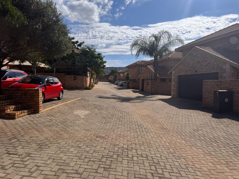 A view of the complex driveway featuring face brick townhouse facades, tiled roofs, and paved access roads.