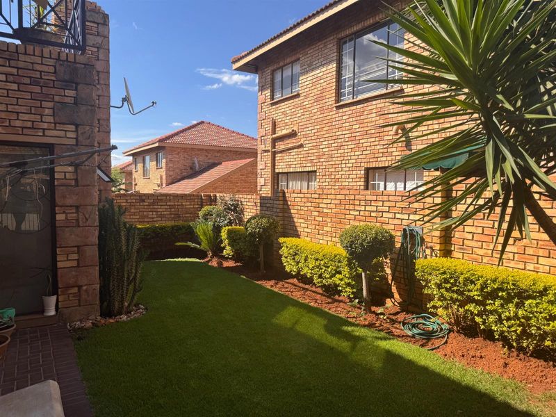 A private rear garden area featuring a well-maintained lawn, landscaped hedges, and a face brick townhouse exterior with paved patio space.