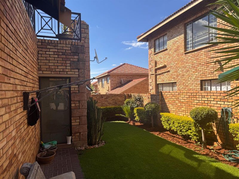 A private rear courtyard featuring face brick townhouse walls, a paved patio area, and a well-maintained artificial lawn with established garden borders.