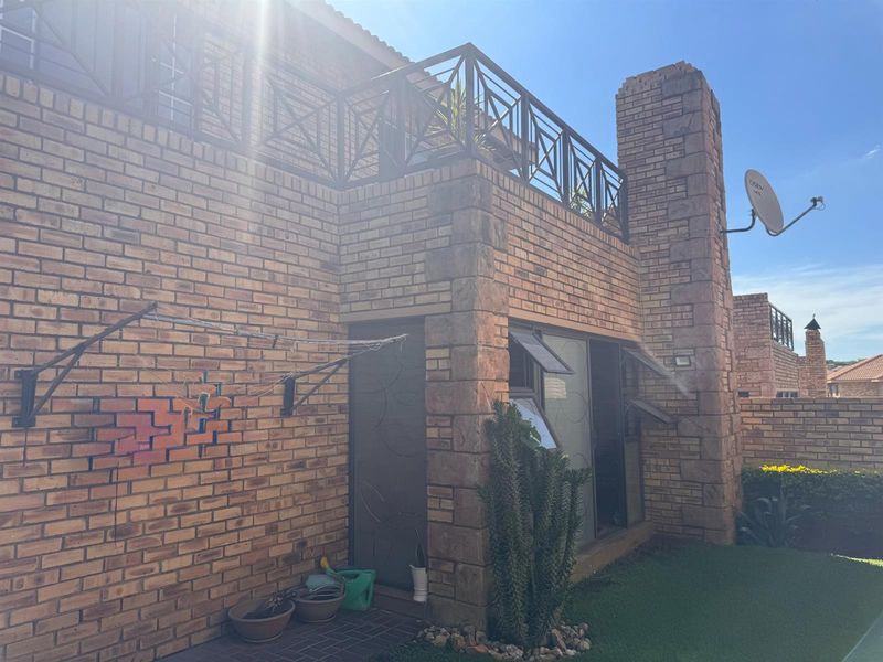 Rear exterior view of a face brick townhouse featuring an upper-level balcony with metal railings, a brick chimney, and wall-mounted washing line.