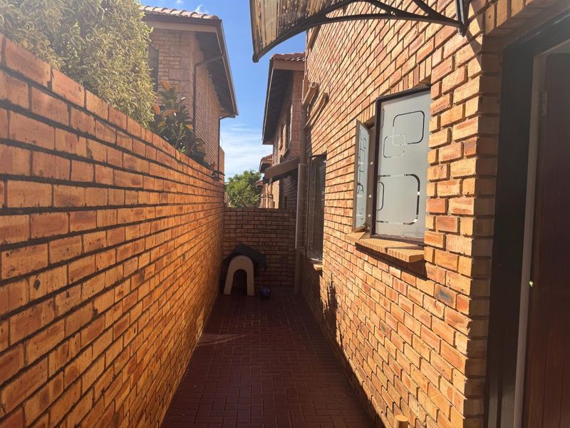 A narrow side passage featuring face brick walls, paved flooring, and a protective awning over the window.