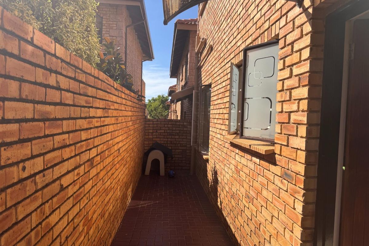 A narrow side passage featuring face brick walls, paved flooring, and a protective awning over the window.
