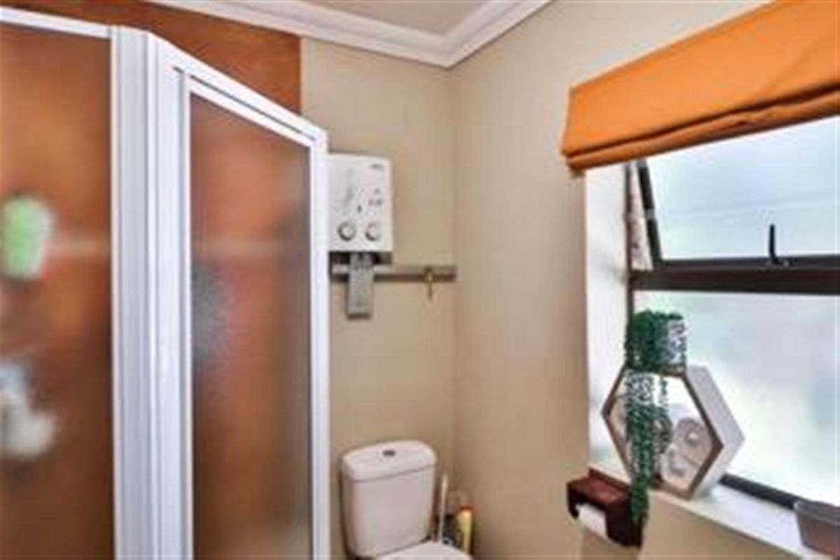 A functional bathroom featuring a shower enclosure, toilet, and wall-mounted water heater, finished with neutral wall tones and a window.