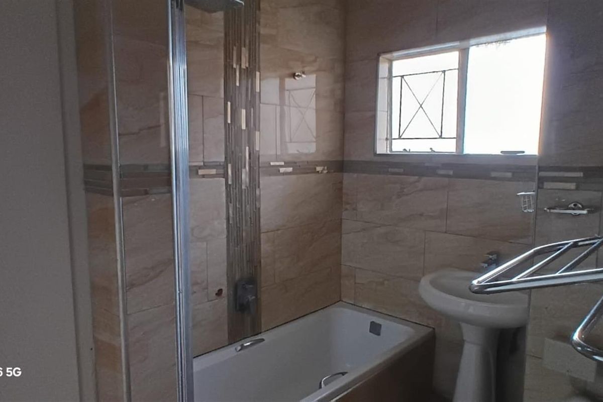A bathroom featuring tiled walls, a bathtub with a glass shower screen, a pedestal basin, and a window with security bars.
