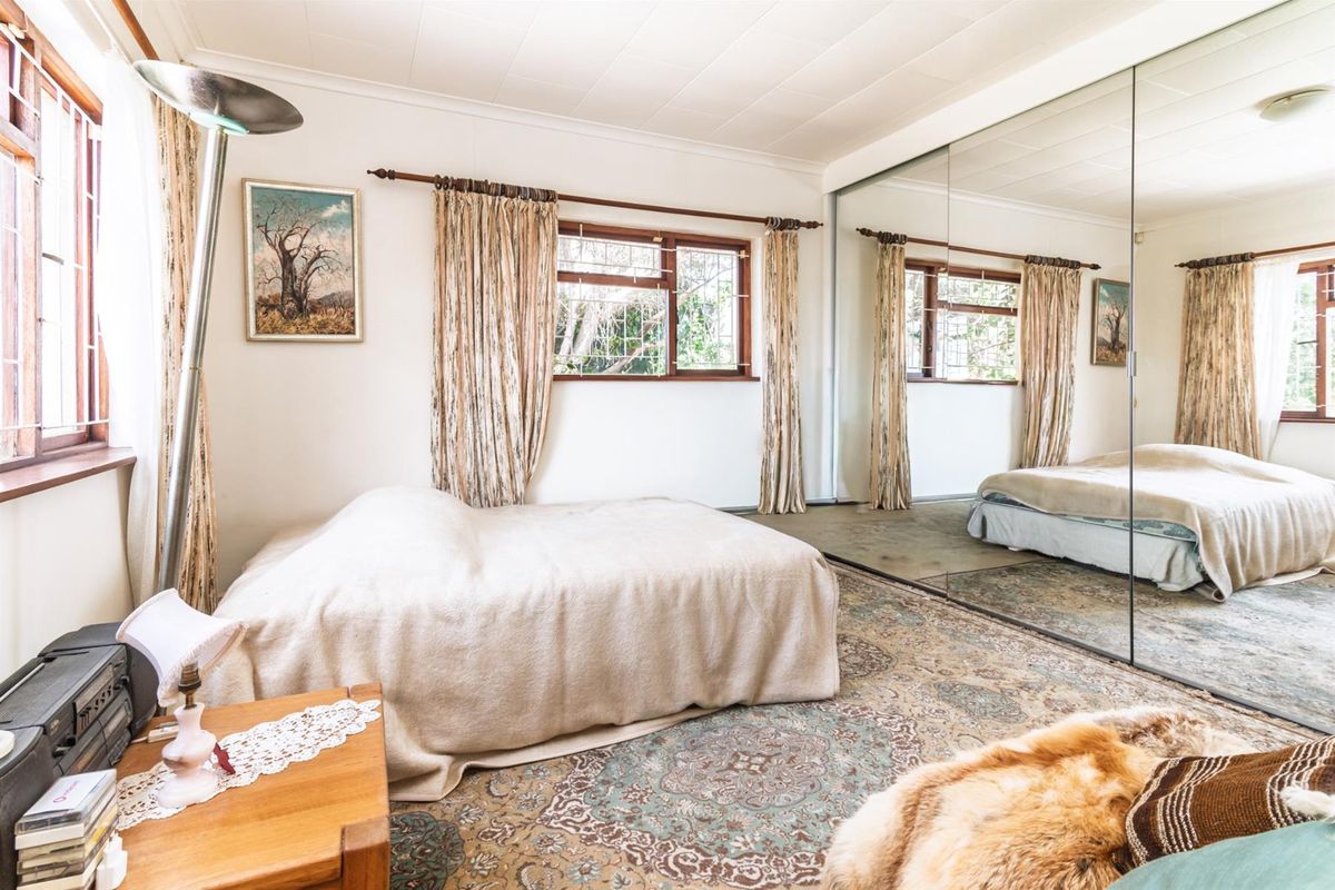 A bedroom featuring large floor-to-ceiling mirrored built-in cupboards and timber-framed windows with security bars.