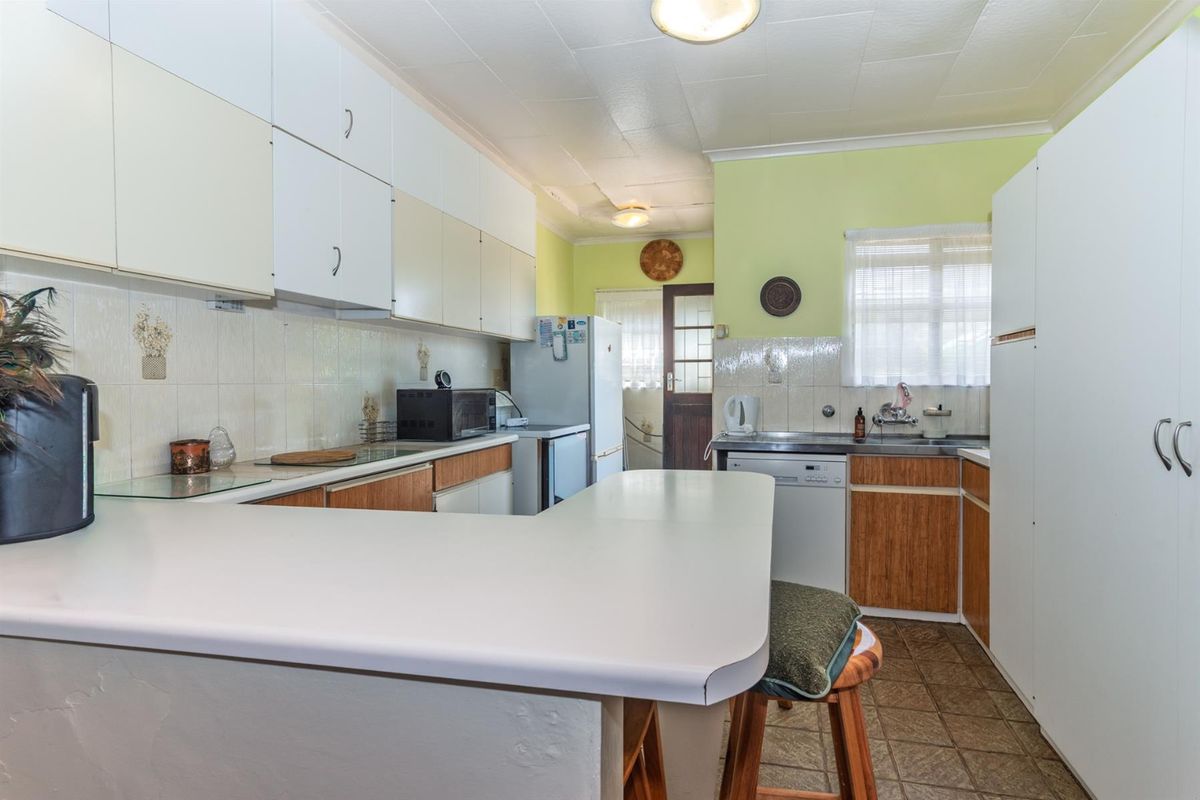 A dated kitchen featuring a breakfast bar, laminate countertops, white upper cabinets, wood-finish lower cabinets, and tiled flooring.