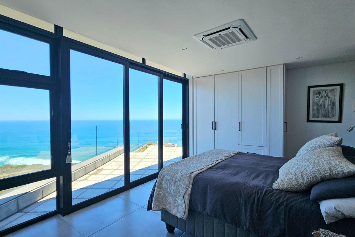 Modern bedroom featuring floor-to-ceiling sliding glass doors with expansive ocean views, integrated ceiling air conditioning, and built-in cabinetry.