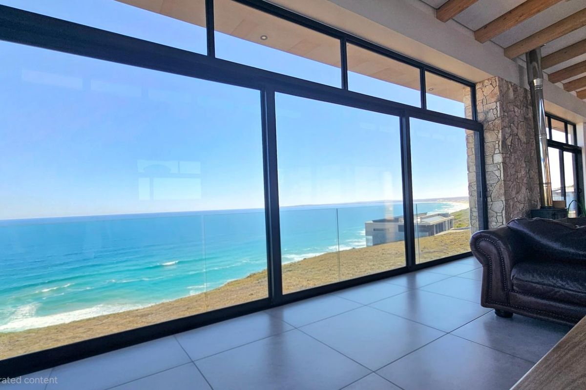 Spacious living area featuring expansive floor-to-ceiling glass sliding doors that frame panoramic ocean views and provide seamless indoor-outdoor flow.