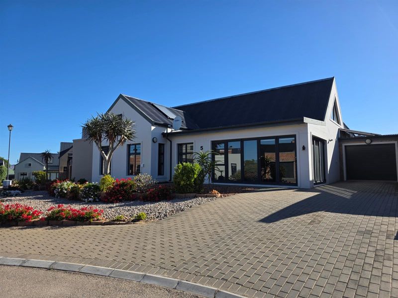 Modern single-story residential home featuring a paved driveway, metal roof, and large aluminium-framed windows and doors.