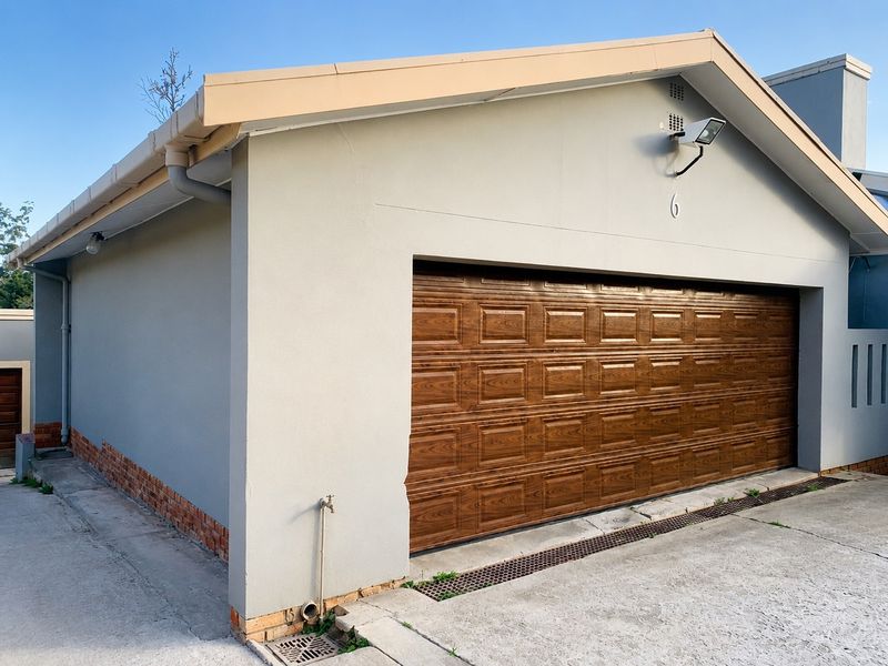 Exterior view of a double garage featuring a wood-look sectional door, exterior lighting, and integrated drainage system.