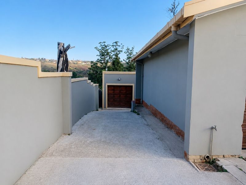 A paved driveway leading to a single garage, flanked by boundary walls and featuring an external water tap and drainage system.