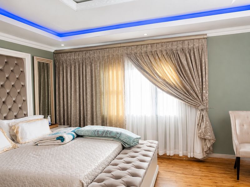 A well-appointed bedroom featuring hardwood flooring, a custom tufted headboard, and a recessed ceiling with integrated blue LED accent lighting.