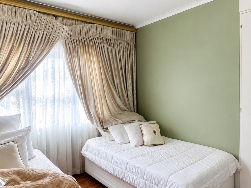 A well-maintained bedroom featuring soft green walls, laminate flooring, and a built-in wardrobe, offering a clean and neutral living space.