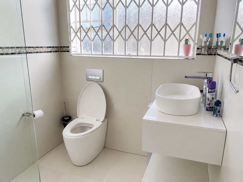 Modern bathroom featuring a wall-mounted toilet, floating vanity with a vessel sink, and a glass-enclosed shower with neutral tiled finishes.