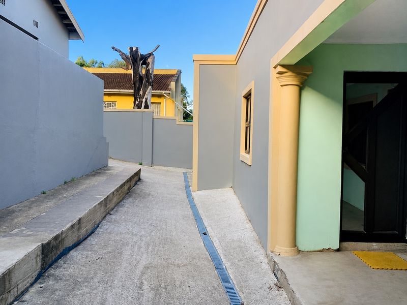 A paved side walkway leading to a covered entrance, featuring a decorative column and integrated drainage channel along the exterior boundary wall.