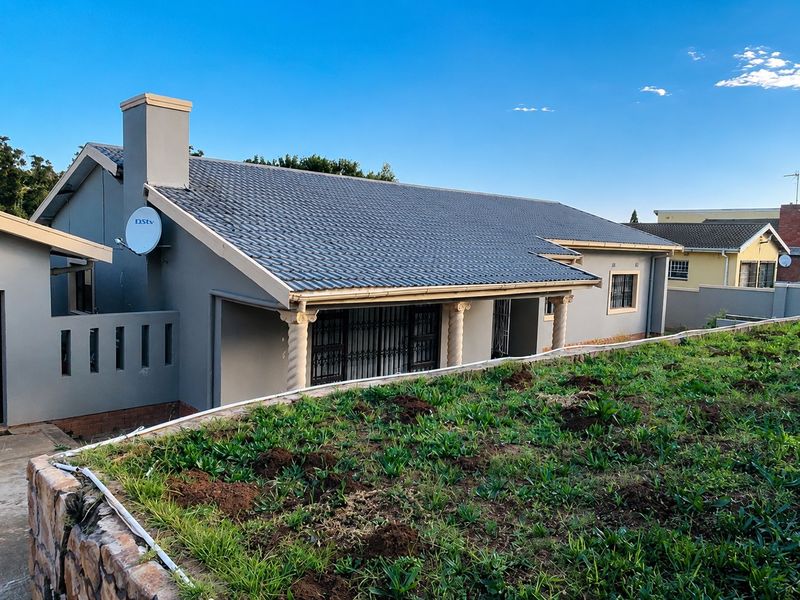 Front elevation of a single-story house featuring a tiled roof, chimney, and decorative columns, set above a stone retaining wall.
