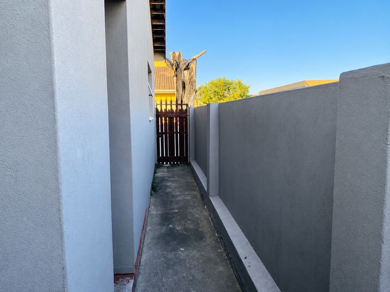 A narrow side passage featuring a concrete walkway, high boundary wall, and a timber gate providing access to the rear of the property.