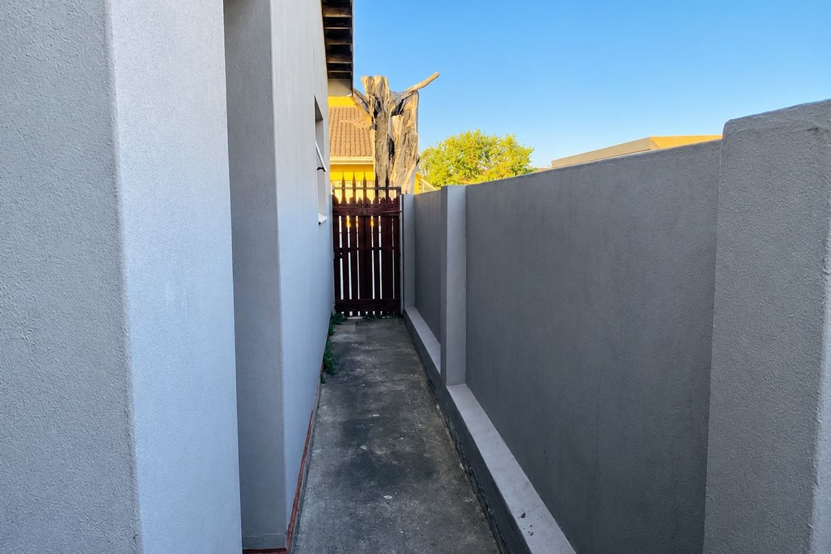 A narrow side passage featuring a concrete walkway, high boundary wall, and a timber gate providing access to the rear of the property.