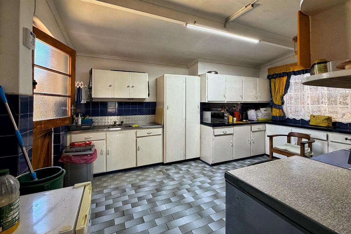 A functional kitchen featuring original built-in cabinetry, laminate countertops, and a tiled backsplash, offering significant potential for a modern renovation.