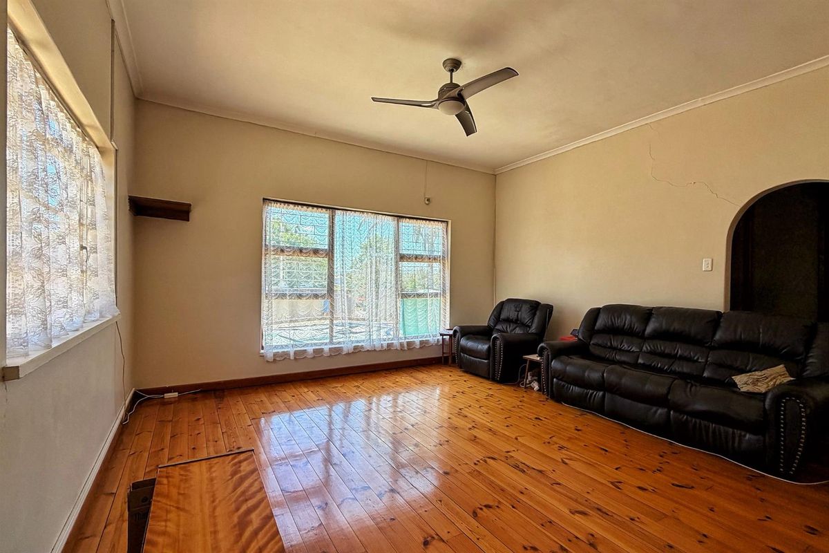 Spacious living room featuring polished hardwood flooring, a ceiling fan, and an arched entryway, with natural light provided by large windows.