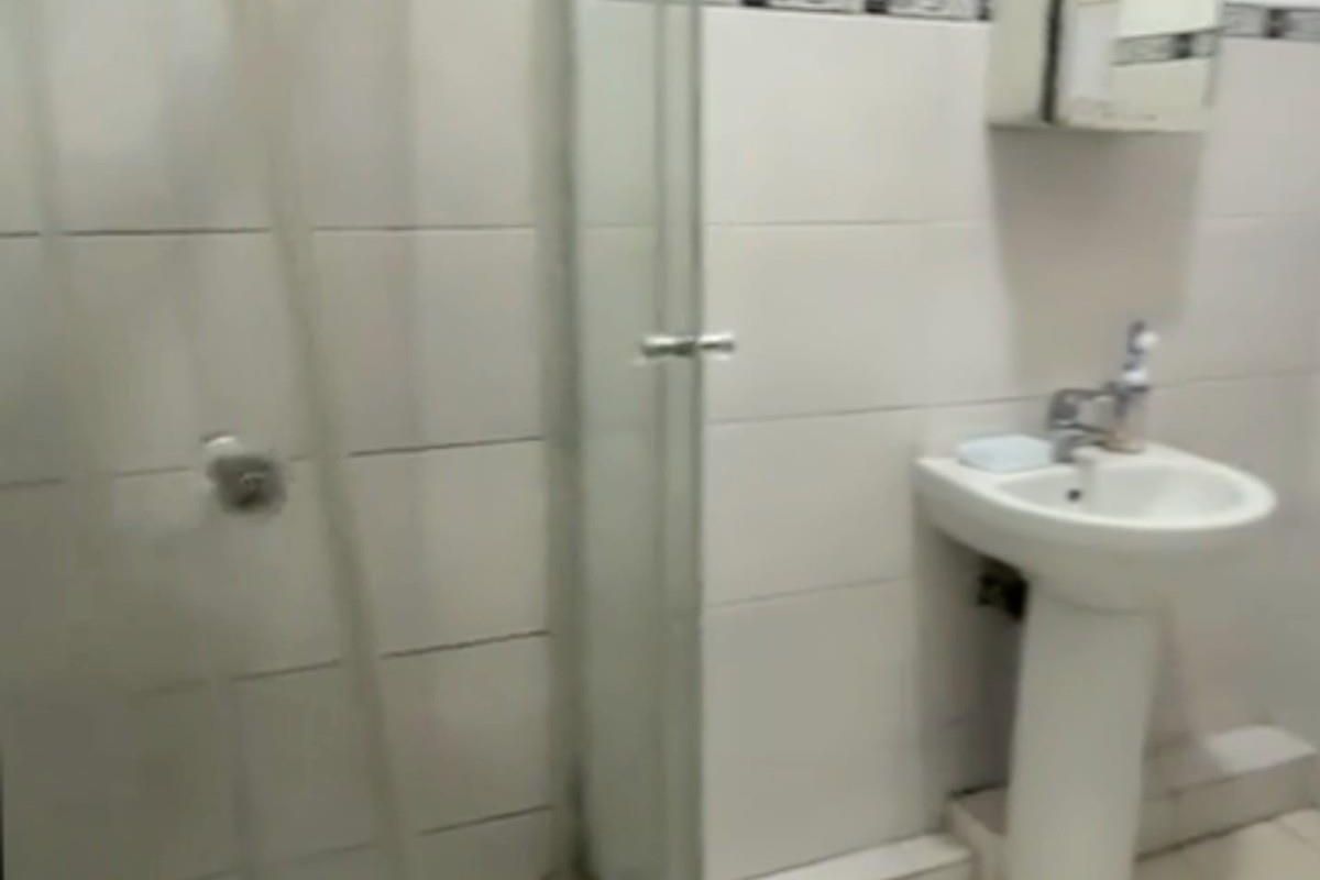 A functional bathroom featuring a glass-enclosed shower, pedestal basin, and wall-mounted medicine cabinet with tiled flooring and walls.