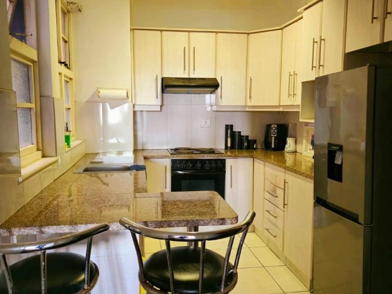 Functional kitchen featuring granite countertops, built-in cabinetry, integrated oven and hob, and tiled flooring, offering a practical layout for daily meal preparation.