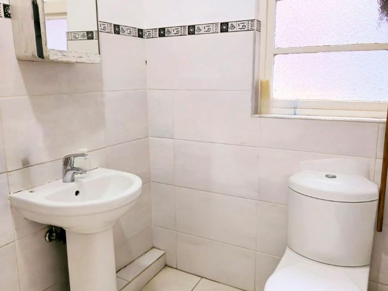 A compact bathroom featuring a pedestal washbasin, toilet, and wall-mounted medicine cabinet with tiled finishes throughout.