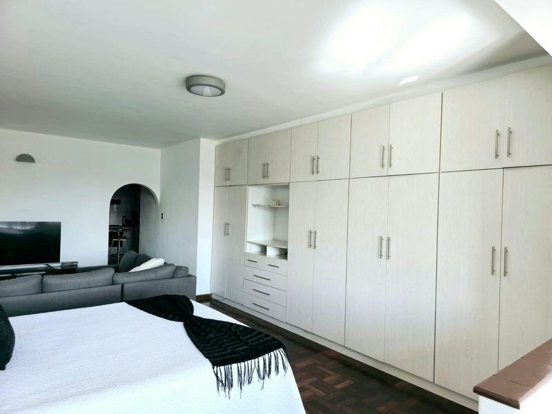 Spacious bedroom featuring extensive built-in cupboards with integrated shelving and drawers, complemented by classic parquet flooring and a distinct arched entryway.
