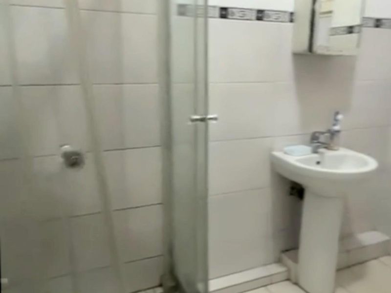A functional bathroom featuring a pedestal basin, shower enclosure, and tiled finishes, currently in need of cosmetic updates.