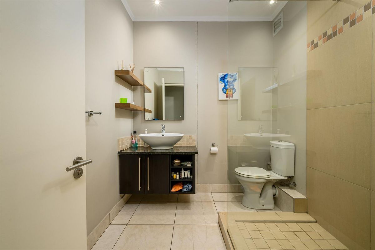 A modern bathroom featuring a floating vanity with a vessel sink, a glass-enclosed shower, and neutral floor-to-ceiling tiling.