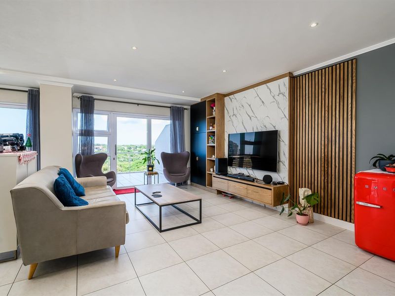 Modern open-plan living area featuring a custom media wall with marble-look paneling, timber slat detailing, and integrated shelving, leading to a private balcony.