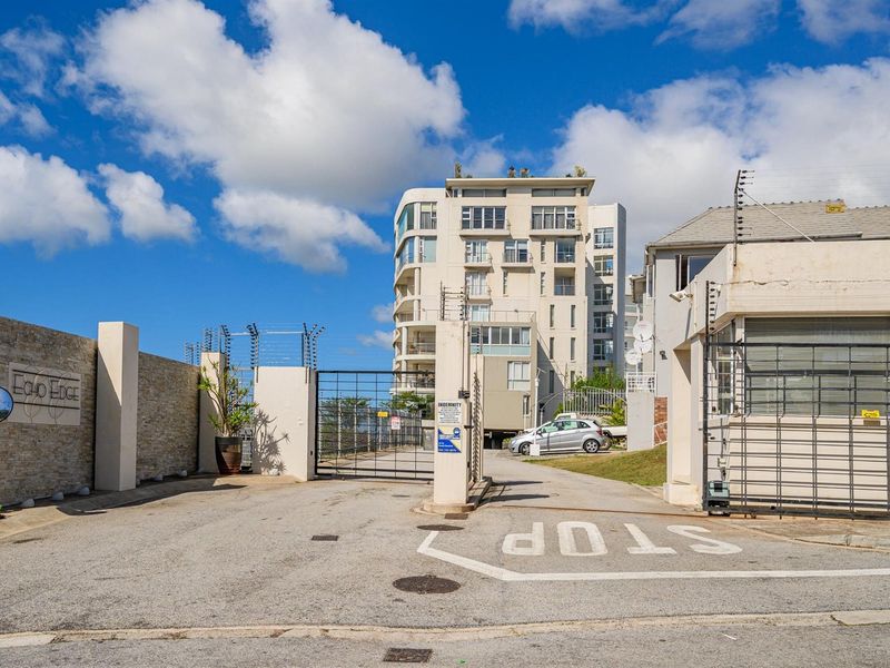 View of the secure gated entrance and driveway leading to the Echo Edge apartment complex, featuring perimeter electric fencing and stone-clad wall detailing.