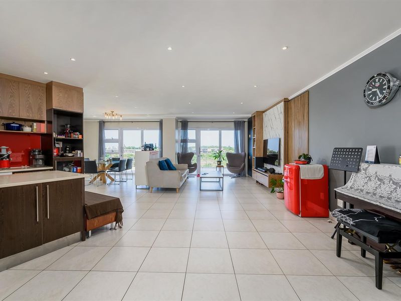 Spacious open-plan living area featuring a modern kitchen with wood-finish cabinetry, tiled flooring, and large sliding doors leading to an outdoor balcony.