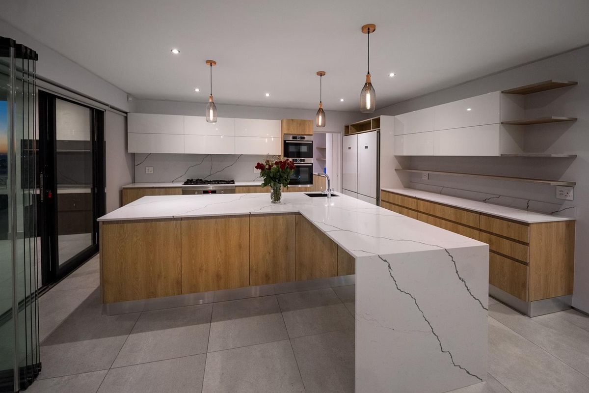 Modern kitchen featuring a large waterfall-edge stone island, integrated cabinetry, built-in oven, and sleek tile flooring with seamless indoor-outdoor flow.
