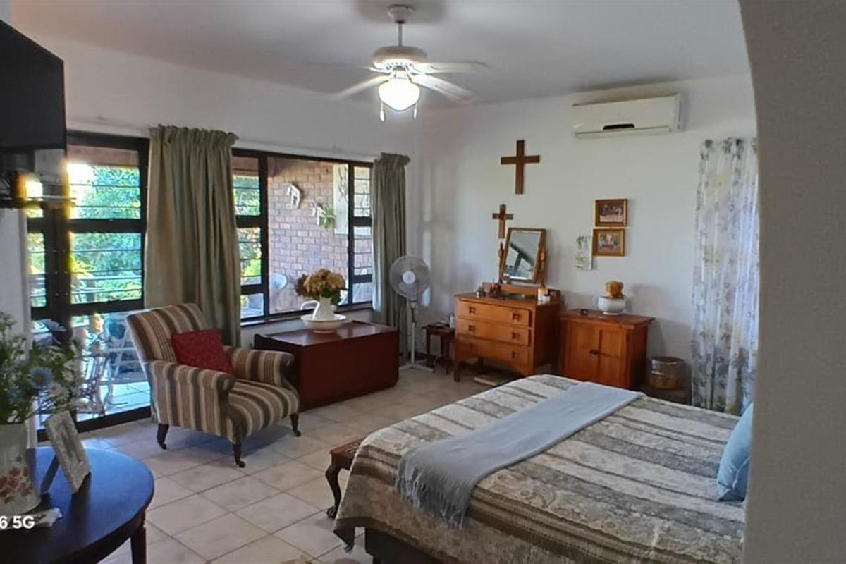 Spacious bedroom featuring tiled flooring, a ceiling fan, and a wall-mounted air conditioning unit, with large windows providing natural light.
