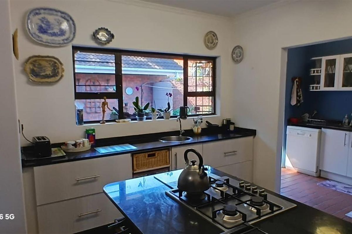 A functional kitchen featuring dark countertops, a central island with a built-in gas hob, and an adjacent scullery area with additional cabinetry.