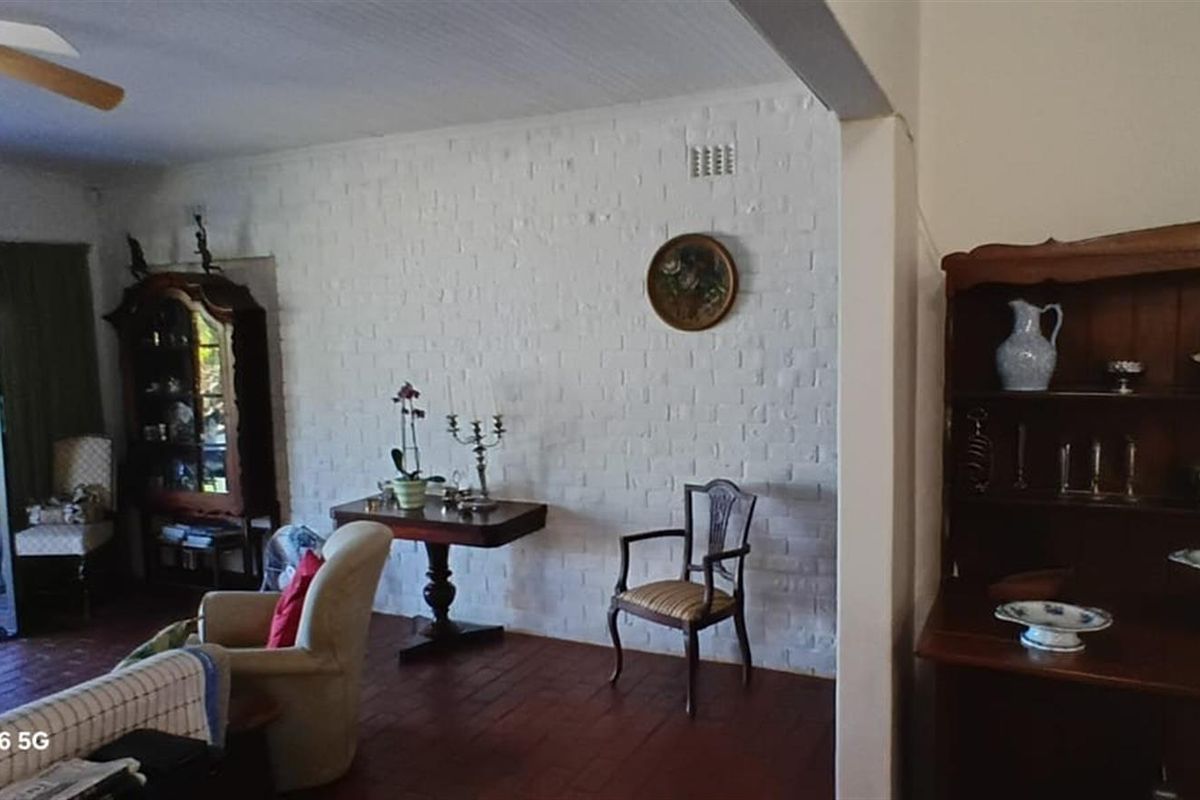 A living room featuring a painted brick feature wall, terracotta tile flooring, and a ceiling fan, with direct access to an outdoor patio area.